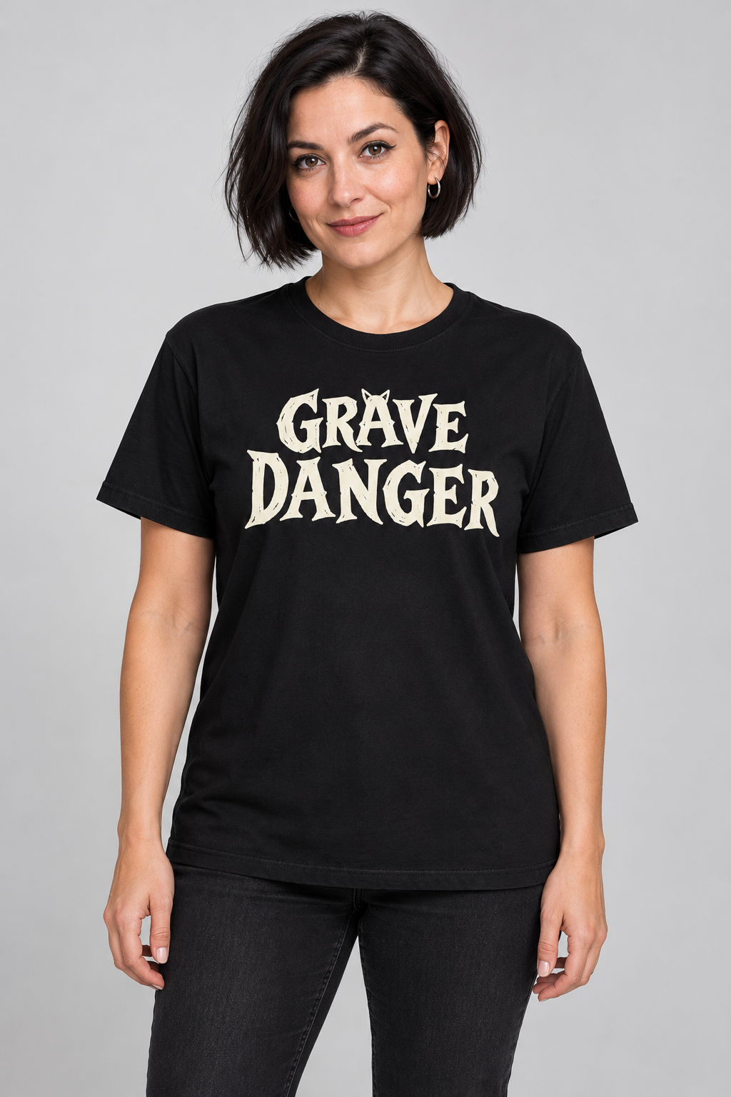 Model displaying front view of grave danger t-shirt, black graphic tee, gothic wordmark front design, black cat grave illustration back, two-sided halloween shirt, spooky cemetery graphic print, cream ink gothic lettering, torn earth night sky design, eerie cat peeking art, unisex crew neck shirt