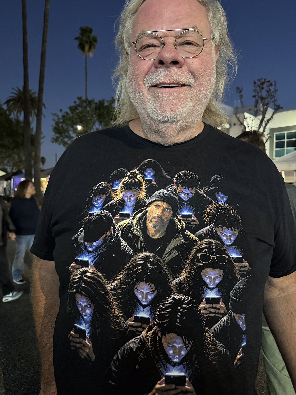 A smiling man with white hair and glasses wearing a scroll zombies t-shirt, black graphic tee, crowd on phones illustration, glowing phone screen design, one person looking up graphic, zombie crowd portrait art, moody high-contrast print, social commentary streetwear graphic, phone addiction satire design, unisex crew neck shirt