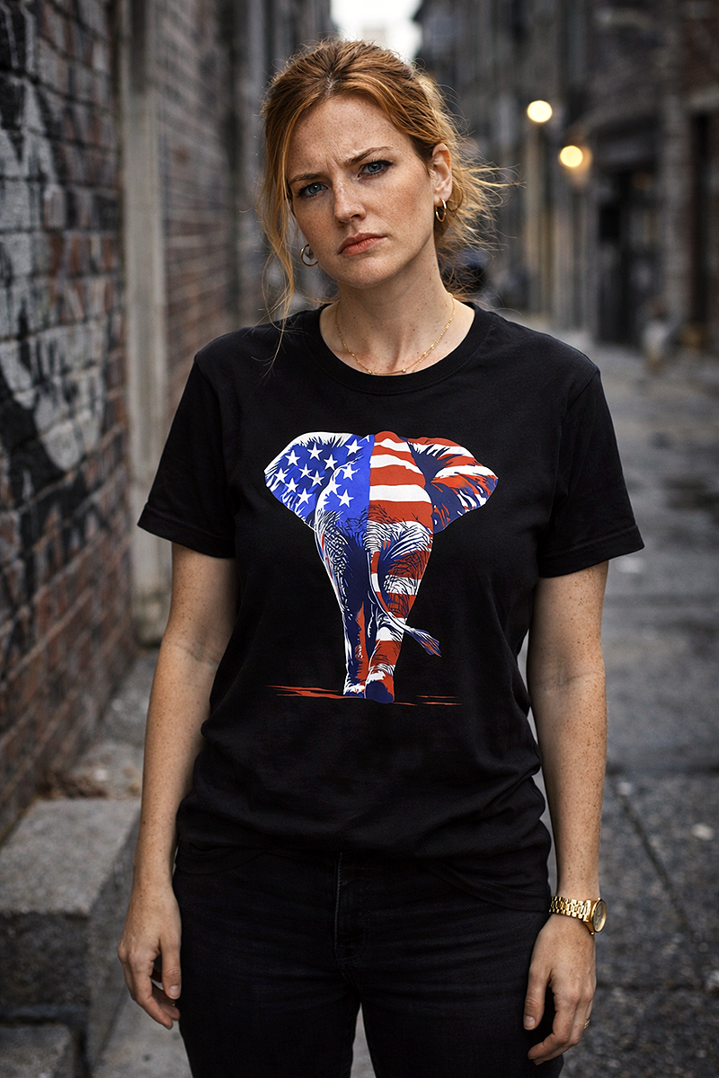 Leaving America Behind Republican elephant American flag political satire tee worn by red-haired female model with stern expression in dark urban alley black t-shirt
