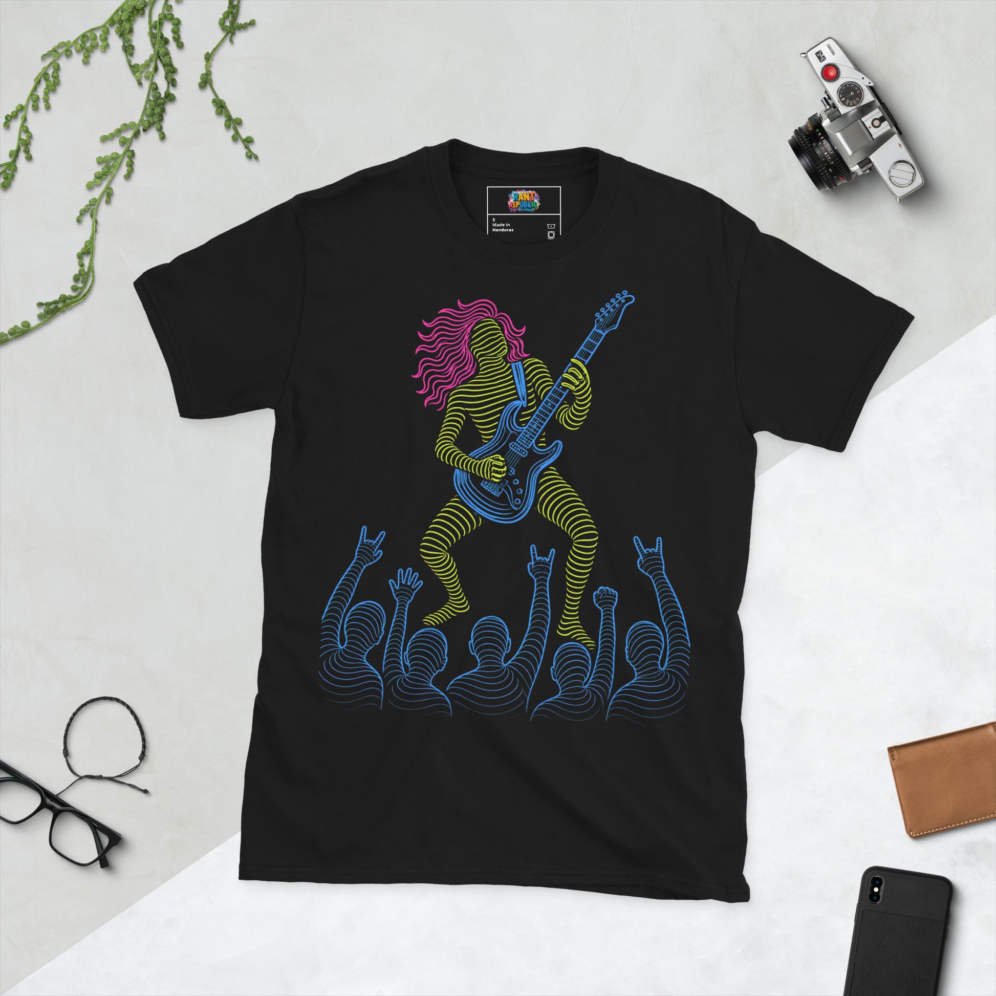 Man wearing a black graphic t-shirt with a neon-lined illustration of a rock guitarist playing to a cheering crowd, glowing yellow, blue, and magenta line art.