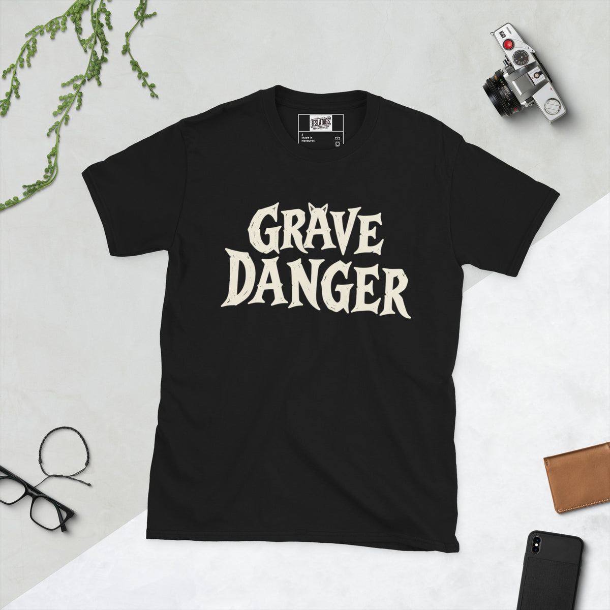 Front view of grave danger t-shirt, black graphic tee, gothic wordmark front design, black cat grave illustration back, two-sided halloween shirt, spooky cemetery graphic print, cream ink gothic lettering, torn earth night sky design, eerie cat peeking art, unisex crew neck shirt